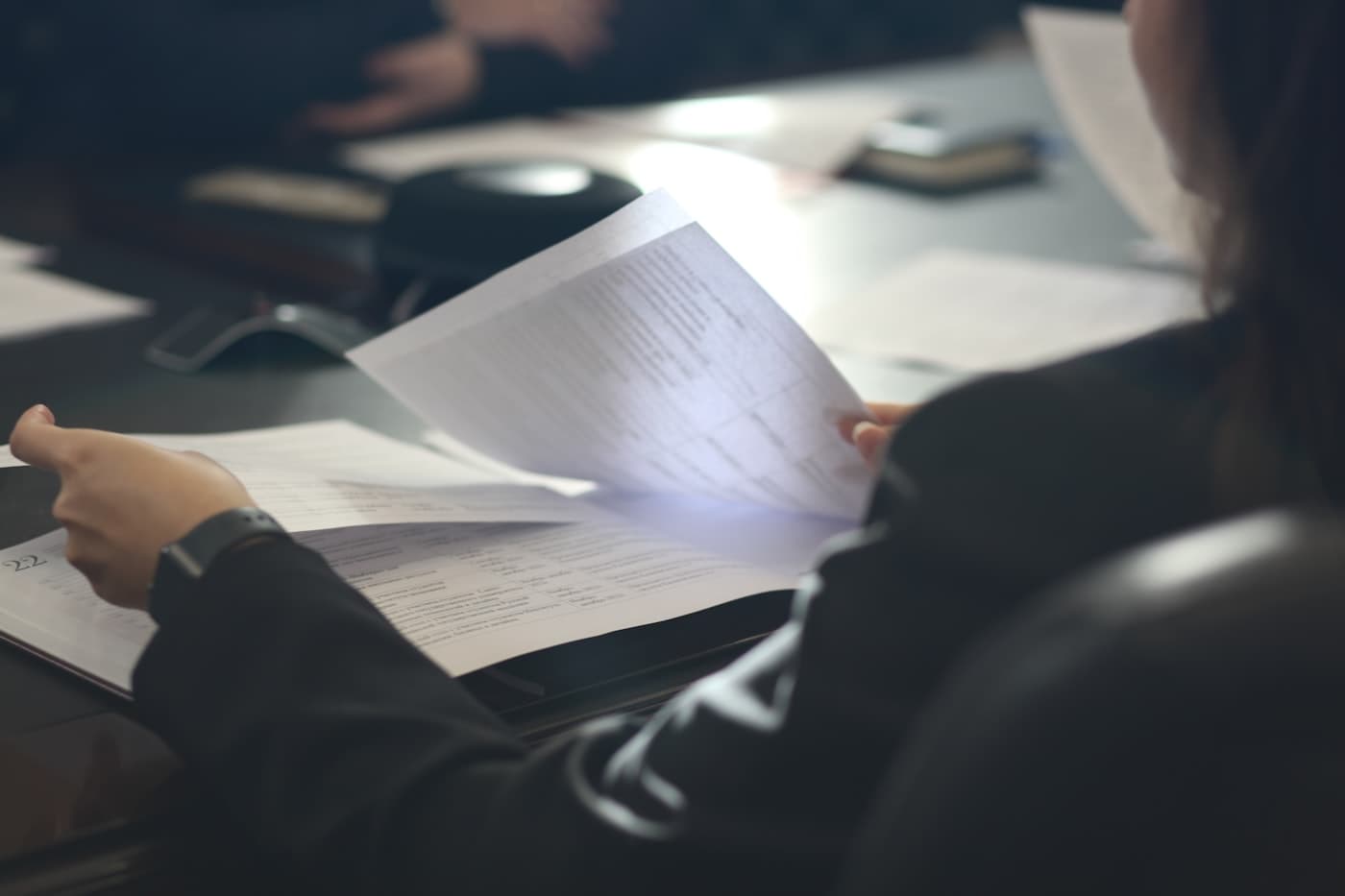 A person reading a printed document closely, glasses in hand, considering what it says.